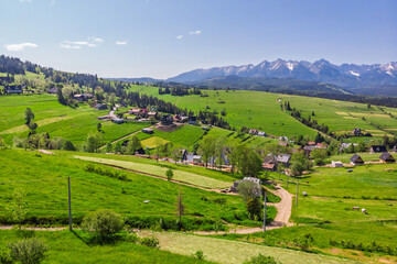 Panoramic view of the snow-capped Tatra Mountains from Rzepiska village in Podhale, Poland. Scenic June landscape with vivid green fields and rural settlement.