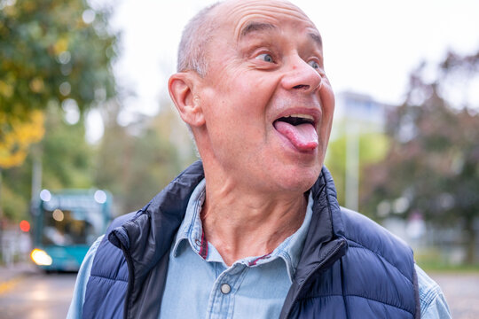 playful older man makes silly face, sticking out tongue and widening eyes in humorous gesture, Expressive facial comedy, Fun and personality, Breaking seriousness, Emotional expression in action