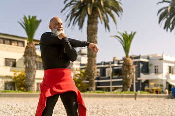 Senior man stretching arm on beach by palm trees