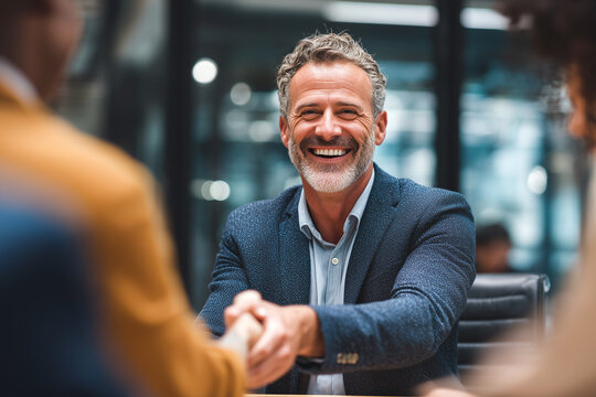 Retrato corporativo que representa conexión profesional, bienvenida y confianza en un entorno colaborativo moderno. Un hombre sonriente estrecha la mano de un compañero en una oficina acristalada