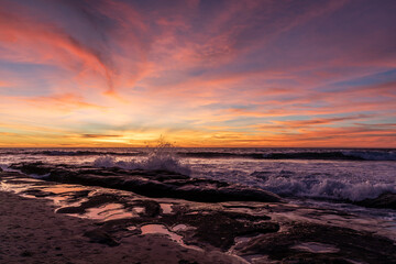 Photograph of wave crashing on rocks under a bright sunset in La Jolla California