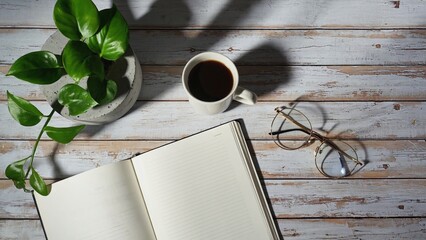 Tranquil study corner with cup of coffee, notebook and glasses on wooden table. Potted plant brings touch of greenery to space. For showcasing peaceful, productive atmosphere or morning routine