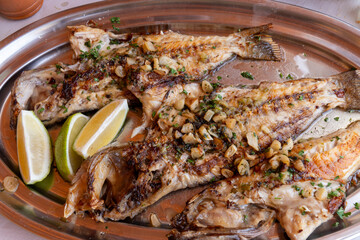 Three grilled fish with fried garlic and olive oil served on a metal platter at a restaurant in Tenerife, Canary Islands, Spain.