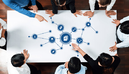 A diverse team engages in a collaborative management meeting, analyzing data networks and digital connections laid out on a white table in a modern office space. Amity