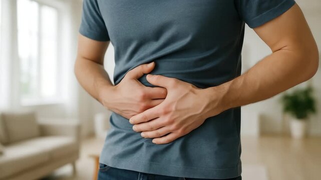 Man in environment living room, holding stomach with both hands. Discomfort and pain, related to gastrointestinal issues. Moment of vulnerability and concern, emphasizing man physical state