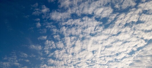 Bright blue sky background with white high-altitude cirrocumulus clouds, suggesting fair weather conditions. Perfect for nature, climate, or background themes. 