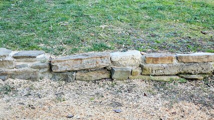 Fototapeta premium Stone wall with grass and dirt ground in outdoor setting 