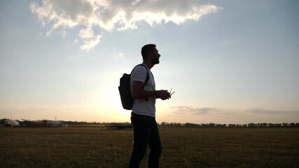 Pilot preparing for flight, focused on remote control, with vast open field and clear sky in background, showcasing the anticipation and excitement of aerial adventure
