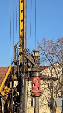 A drilling rig at an urban construction site on a sunny day. Close-ups of the equipment components, metal cables, hydraulics, and drilling mechanism. Industrial theme: construction, engineering