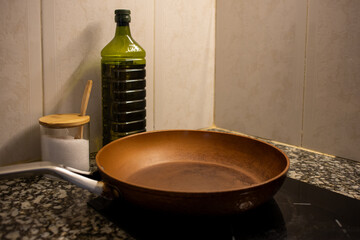 Frying pan on stove close-up, salt, oil in bottle on table.