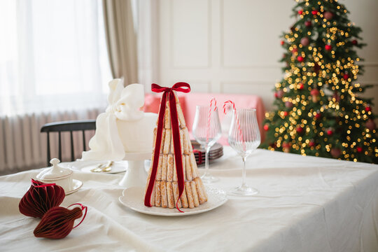 Croquembouche style dessert with sponge fingers on a dining table in front of an illuminated Christmas tree