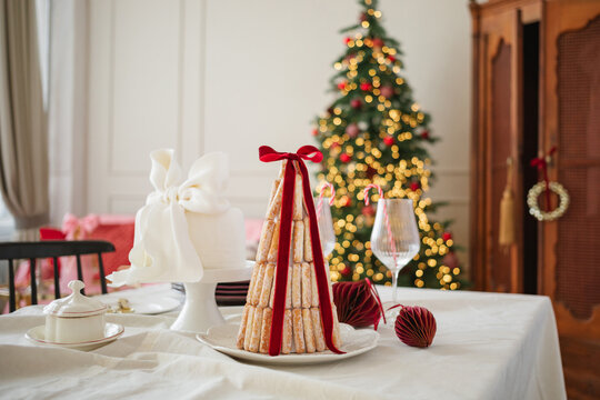 Croquembouche style dessert with sponge fingers on a dining table in front of an illuminated Christmas tree