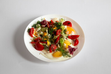 Scrambled eggs with vegetables and herbs on a plate on a white background