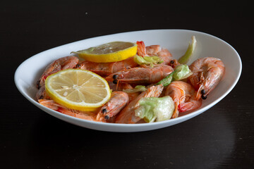 White plate with shrimp and lemon on a black table