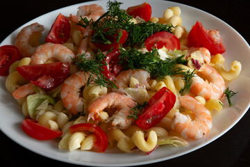 Pasta with shrimp, vegetables and herbs on a plate on a black background