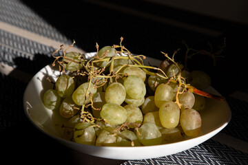 A white plate with grapes on the table illuminated by sunlight