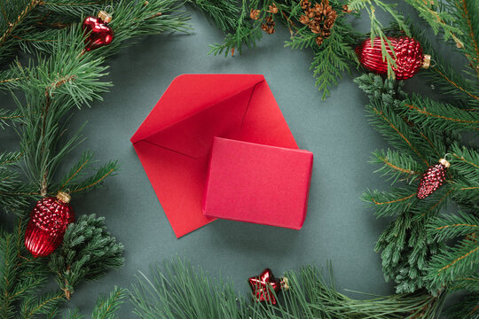 Overhead view of a red gift box and an envelope surrounded by assorted Christmas baubles and fir branches on a green background