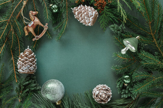 Overhead view of fir branches with Christmas bubbles and ornaments arranged as a border on a green background