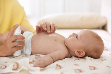 Mother applying cream onto her baby's body on bed at home, closeup