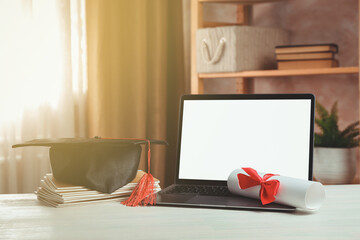 Diploma, graduation cap, stacked copybooks and laptop on white wooden table indoors
