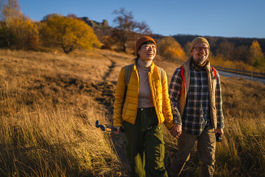 Mature couple hiking through autumn field holding hands