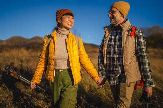 Mature couple hiking through autumn field holding hands