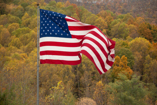 Aerial view of an American flag blowing in the wind above the trees in an autumnal mountain landscape, USA