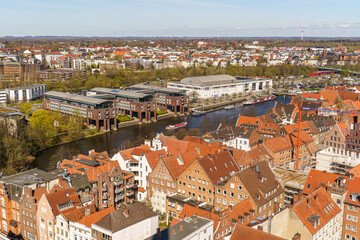 Obraz premium A Lubeck city view in Germany with many buildings and a river. The buildings are mostly red and brown. The sky is blue and the sun is shining