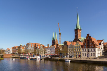 Obraz premium A panoramic view of houses on the waterfront in Lubeck, Germany The dock accommodates many small boats and ships. The weather is sunny and clear, with a blue sky
