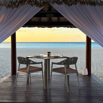 Private dining table set up in a beach cabana at sunset, Eagle Beach, Aruba