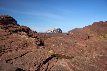 Seacliff Beach, East Lothian, offers rugged red rock formations. A distant Bass Rock rises over the sea.