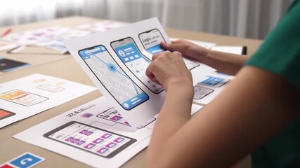 Startup company employee planning for user interface prototype for mobile application or website in office with model of program on desk. UX UI designer consider user friendly interface plan. Synergic