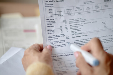 Adult woman holding pen reviewing utility bill and invoice documents at desk, focusing on analyzing charges and payment details, hands in close up