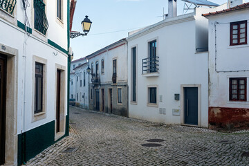 Scenic cobblestone street lined with whitewashed houses and balconies in historic Portuguese town, tranquil residential architecture and urban atmosphere