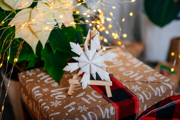 A decorative white 3D snowflake displayed on a small wooden easel placed on a wrapped Christmas gift with glowing fairy lights.