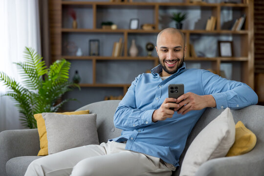 Smiling man relaxing on sofa using smartphone for communication