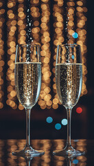 Two champagne flutes filled with sparkling wine, with a bokeh background of warm lights.