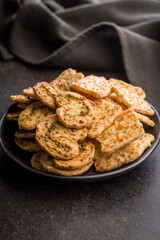 Crunchy salted crackers on plate on black table.