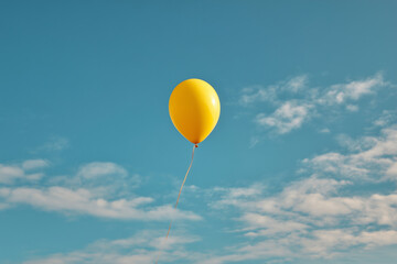 A yellow balloon is floating in the sky above a blue sky