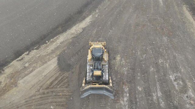 Aerial drone view of a large tracked tractor leveling soil on an open site, showing precise earthmoving, heavy power, and industrial efficiency in large-scale ground preparation.