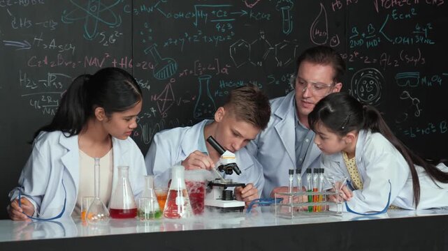 Multicultural student looking under microscope while cute girl inspect sample. Teacher looking after high school children doing experiment at blackboard with science theory in STEM class. Edification - Powered by Adobe