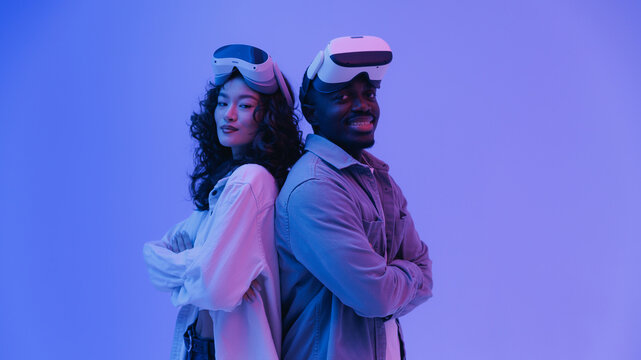 Portrait happy African male and Asian female diverse adults enjoying virtual reality headsets in neon lighting - Powered by Adobe
