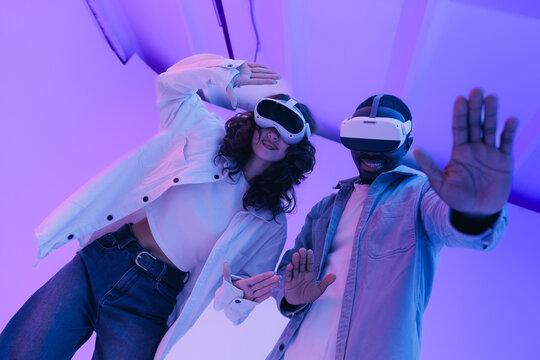 Young multiethnic team adults experiencing virtual reality with headsets in neon lighting. Fashion Immersive and futuristic innovation technology with AI. - Powered by Adobe