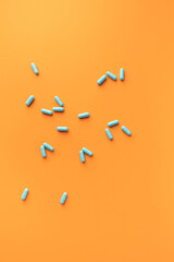 Blue, turquoise capsules on an orange background. Vertical.