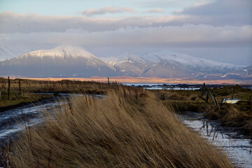 Muddy rural road and snowy mountains near Akranes, Iceland