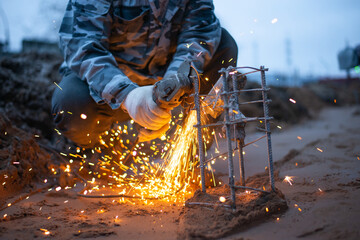 A person saws a reinforcing cage for a future concrete structure. Construction site in the evening. High quality photo
