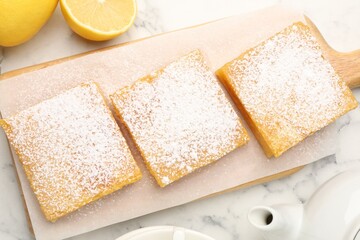 Tasty lemon bars with powdered sugar and fresh fruits on white marble table, flat lay