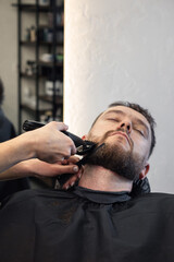 Barber wielding electric hair clipper shaving beard customer in modern barbershop. Bearded Man client visit gentleman grooming beauty salon for hairstyle care. Male beard style concept