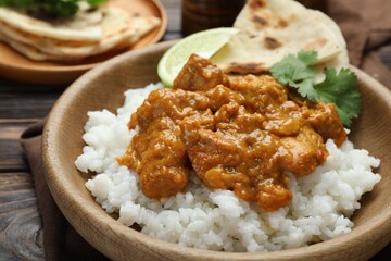 Delicious chicken tikka masala with rice, cilantro, lime and lavash in bowl on wooden table, closeup