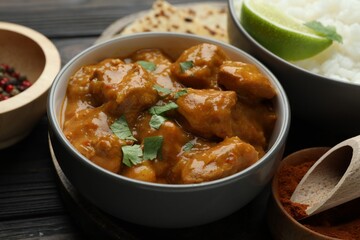Delicious chicken tikka masala, rice, cilantro, lime and spices on wooden table, closeup